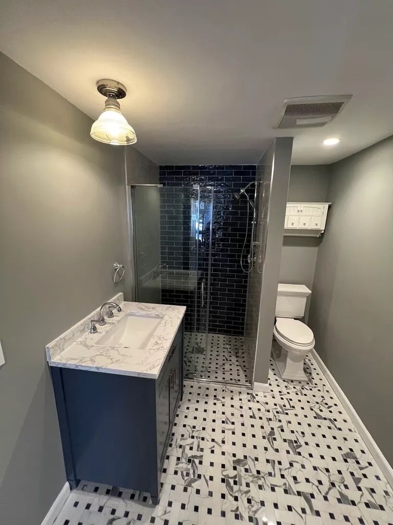 Black subway tile bath — full view with navy vanity and basketweave floor