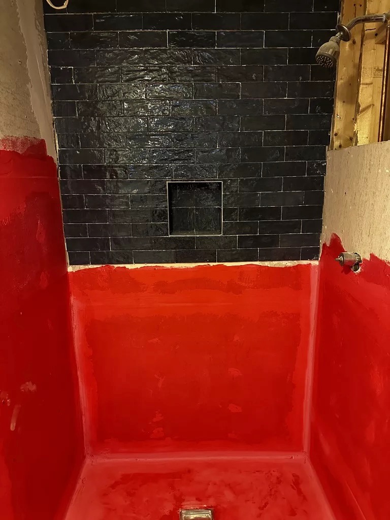 Shower waterproofing — red membrane with black tile mid-install